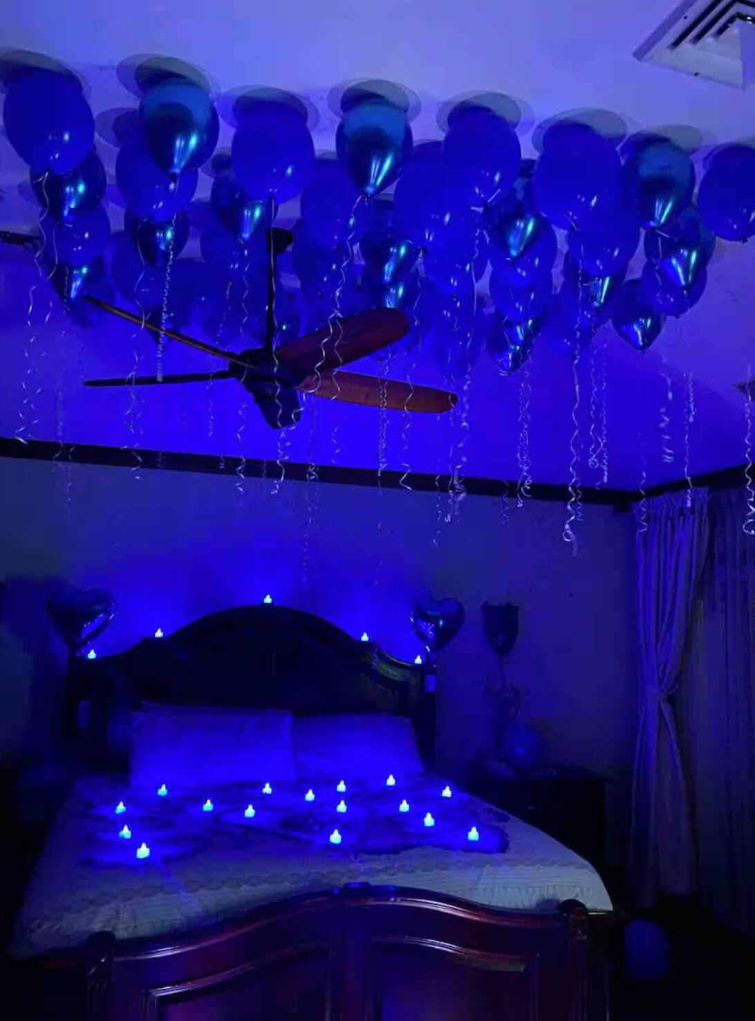 A bedroom with a bed, a ceiling fan, and blue lighting.