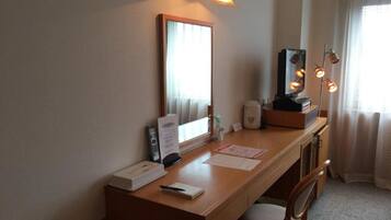 A hotel room with a wooden desk, a mirror, a lamp, and a chair.