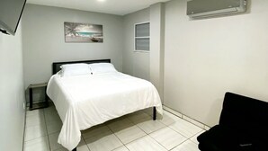 A bedroom with a bed, a TV mounted on the wall, an air conditioner, and a small table. - Apartment Rio Nigua  (Salinas)
