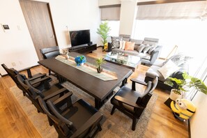 A modern living room with a dark wooden dining table, black chairs, a glass coffee table, a grey sofa, and a television.