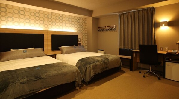 Habitación de hotel con dos camas, un escritorio, una silla y una pequeña mesa con una computadora.