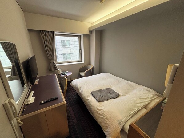 Una habitación de hotel con cama, escritorio y silla, televisión y ventana con cortinas.