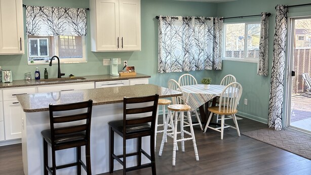 A kitchen with a central island, white cabinets, and a dining area with a table and chairs. - Cozy Home in Historic Helper Utah, near park, pool, Utah Aggies baseball field. (Helper)