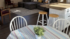 A cozy living room with a sectional sofa, a dining table with chairs, a small kitchen area, and a ceiling fan. - Cozy Home in Historic Helper Utah, near park, pool, Utah Aggies baseball field. (Helper)