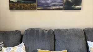 A living room with a grey sofa, three framed landscape paintings on the wall, and a cushion with the text "together our favorite place to be". - Cozy Home in Historic Helper Utah, near park, pool, Utah Aggies baseball field. (Helper)