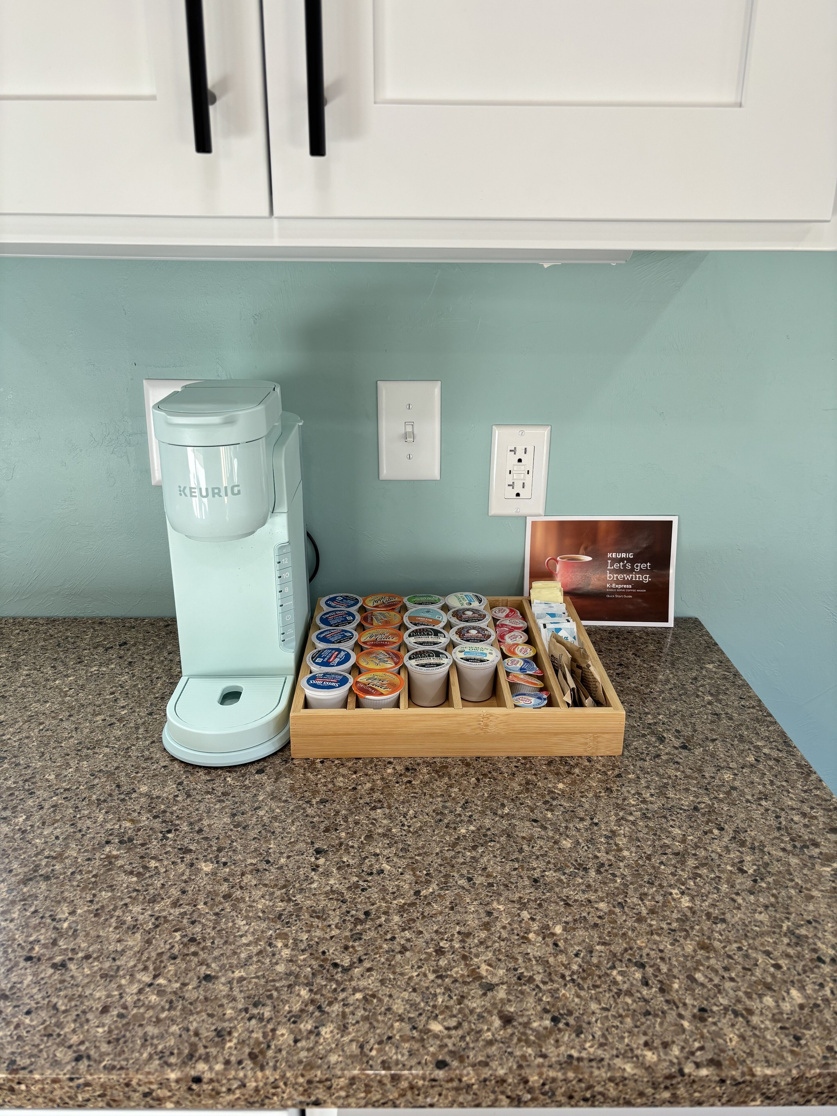 Una cafetera Keurig sobre una encimera de granito con un portal cápsulas de café que contiene varias cápsulas.