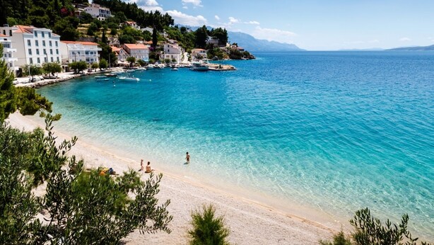 A coastal town with a clear blue sea, sandy beach, and buildings along the shore.