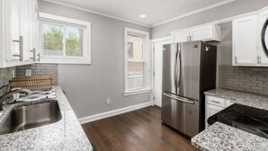 A modern kitchen with white cabinets, a stainless steel refrigerator, granite countertops, and a wooden floor.