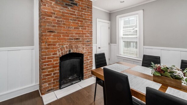 A dining room with a brick fireplace, white paneled walls, a wooden table, and black chairs.