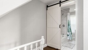 A room with a white wardrobe, a wooden staircase, and a bathroom with a shower curtain.