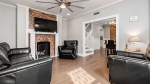 A living room with a fireplace, leather sofas, a TV, and a ceiling fan.
