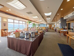 A spacious hotel dining area with a buffet setup, large windows, and a view of the cityscape.