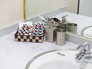Une salle de bain dotée d’un comptoir en marbre, d’un lavabo, d’un miroir et d’articles de toilette, notamment un porte-brosse à dents et des gobelets.