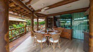 A wooden deck with a dining table and chairs, surrounded by glass doors and windows. - Bangalô 08 - Ilhabela (Ilhabela)
