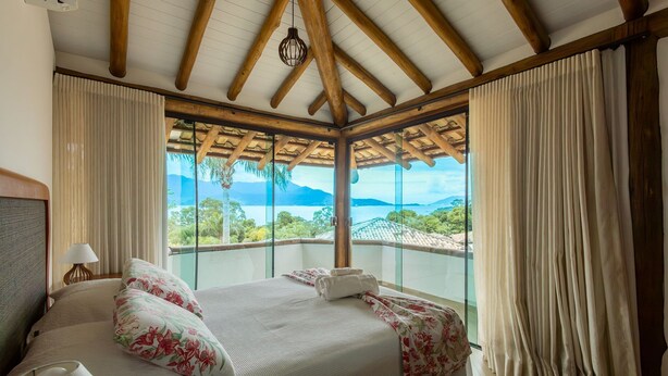 A hotel room with a large bed, a view of the mountains, and a balcony with curtains. - Bangalô 08 - Ilhabela (Ilhabela)