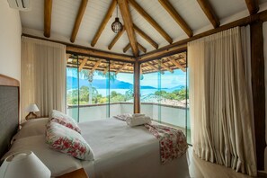 A hotel room with a large bed, a view of the mountains, and a balcony with curtains. - Bangalô 08 - Ilhabela (Ilhabela)