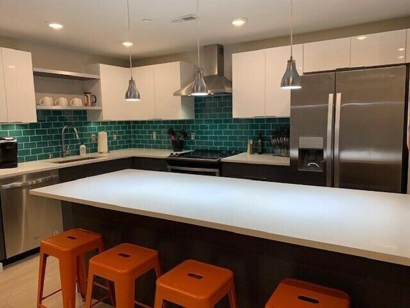 A modern kitchen with a large island, stainless steel appliances, and orange bar stools.