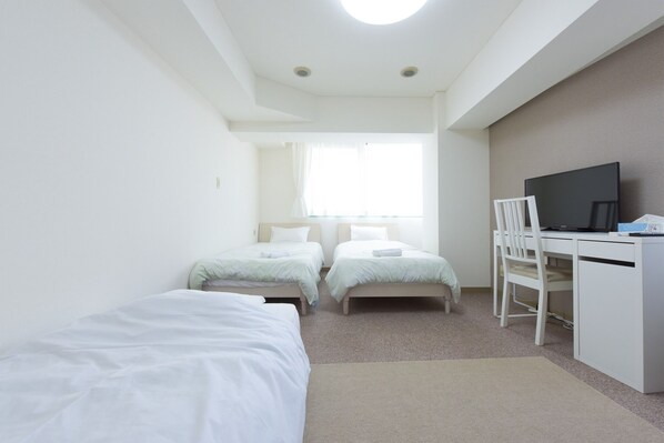 A small, clean room with two single beds, a desk with a chair, and a television.