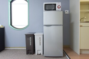 Una kitchenette compacta con microondas, dos cubos de basura y una ventana.