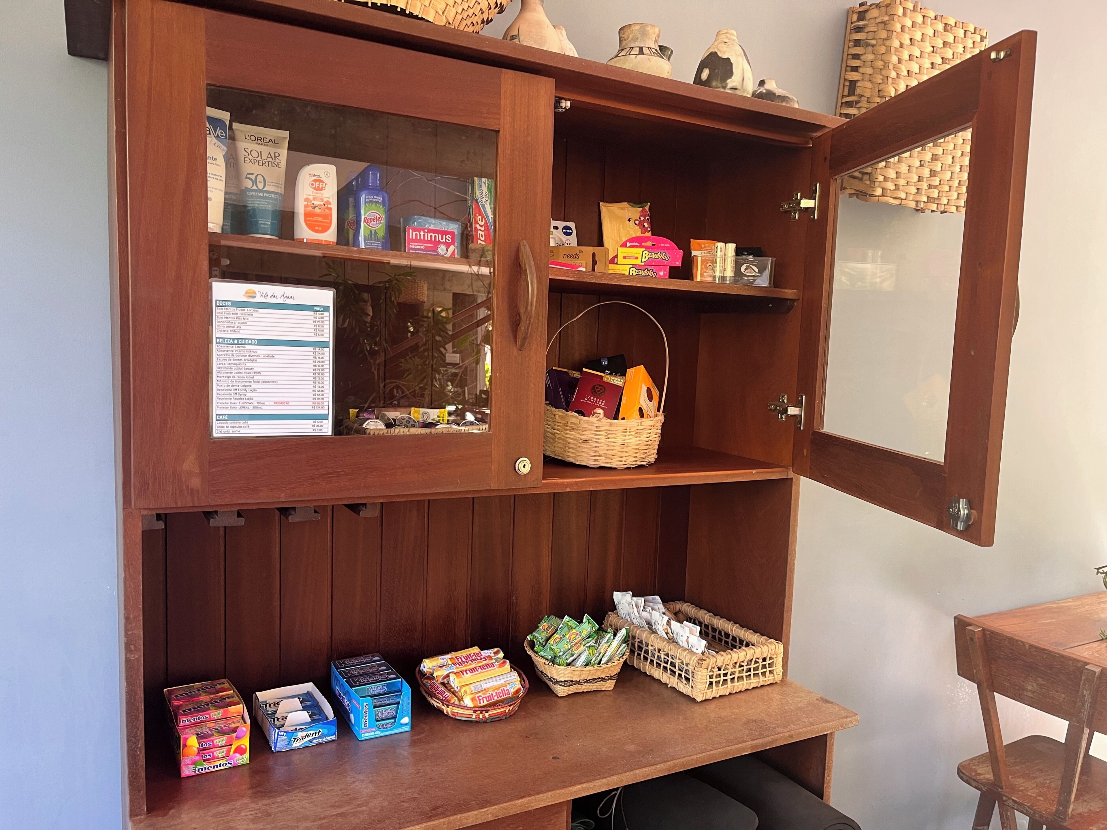 Un mueble de madera con puertas de cristal que exhibe artículos de aseo, un menú y una cesta con libros y una billetera.