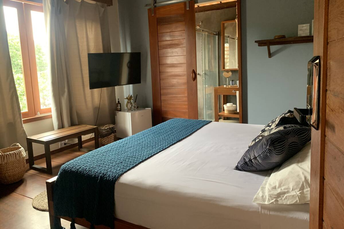 Een slaapkamer met een bed, een televisie, een houten garderobe, een klein tafeltje en een raam met gordijnen.