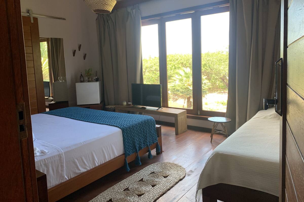 Een hotelkamer met een groot bed, een bureau met een televisie, een kleintje tafel en uitzicht op groen buiten de ramen.