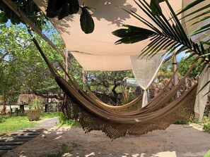 A hammock under a canopy in a garden setting with a pathway and potted plants. - Vila das Águas Atins (Barreirinhas)