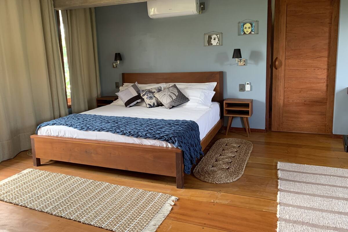 Een slaapkamer met een houten bed, een blauwe deken, een geweven vloerkleed en een nachtkastje van hout.