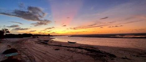 Una playa con atardecer, terreno arenoso y algunas embarcaciones.