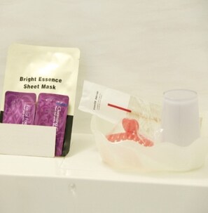 Una estant amb un paquet de màscara facial Bright Essence i un petit recipient amb un objecte vermell.