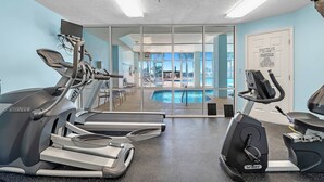 A gym with treadmills, an elliptical, and a pool area visible through glass doors. - 401 Dunes at the end of Fort Morgan Road (Gulf Shores)