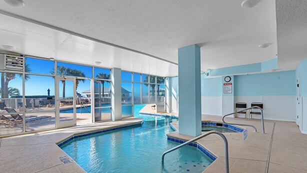 An indoor swimming pool with clear glass walls, a tiled floor, and a lifeguard chair. - 401 Dunes at the end of Fort Morgan Road (Gulf Shores)