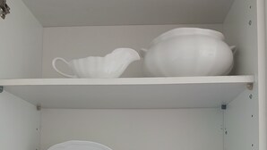 Un armario blanco con estantes que contienen platos, tazones y una tetera blancos.
