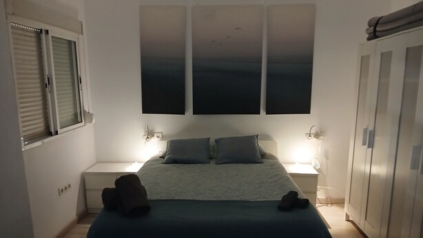 Un dormitorio con cama, dos mesitas de noche, un armario y una ventana con persianas.