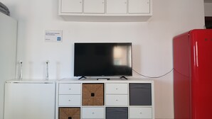 Habitación con un armario blanco sobre un televisor de pantalla plana, un refrigerador rojo y un cartel que indica estudio con escritorio.