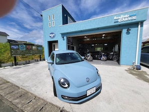 Um edifício azul claro com placa de garagem, um carro estacionado e motocicletas dentro.