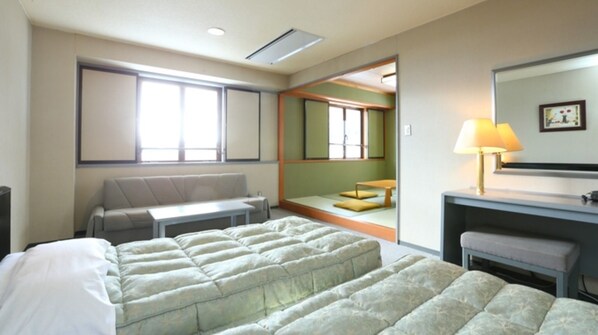 Quarto de hotel com cama, escrivaninha, cadeira, sofá, luminária e uma janela grande.