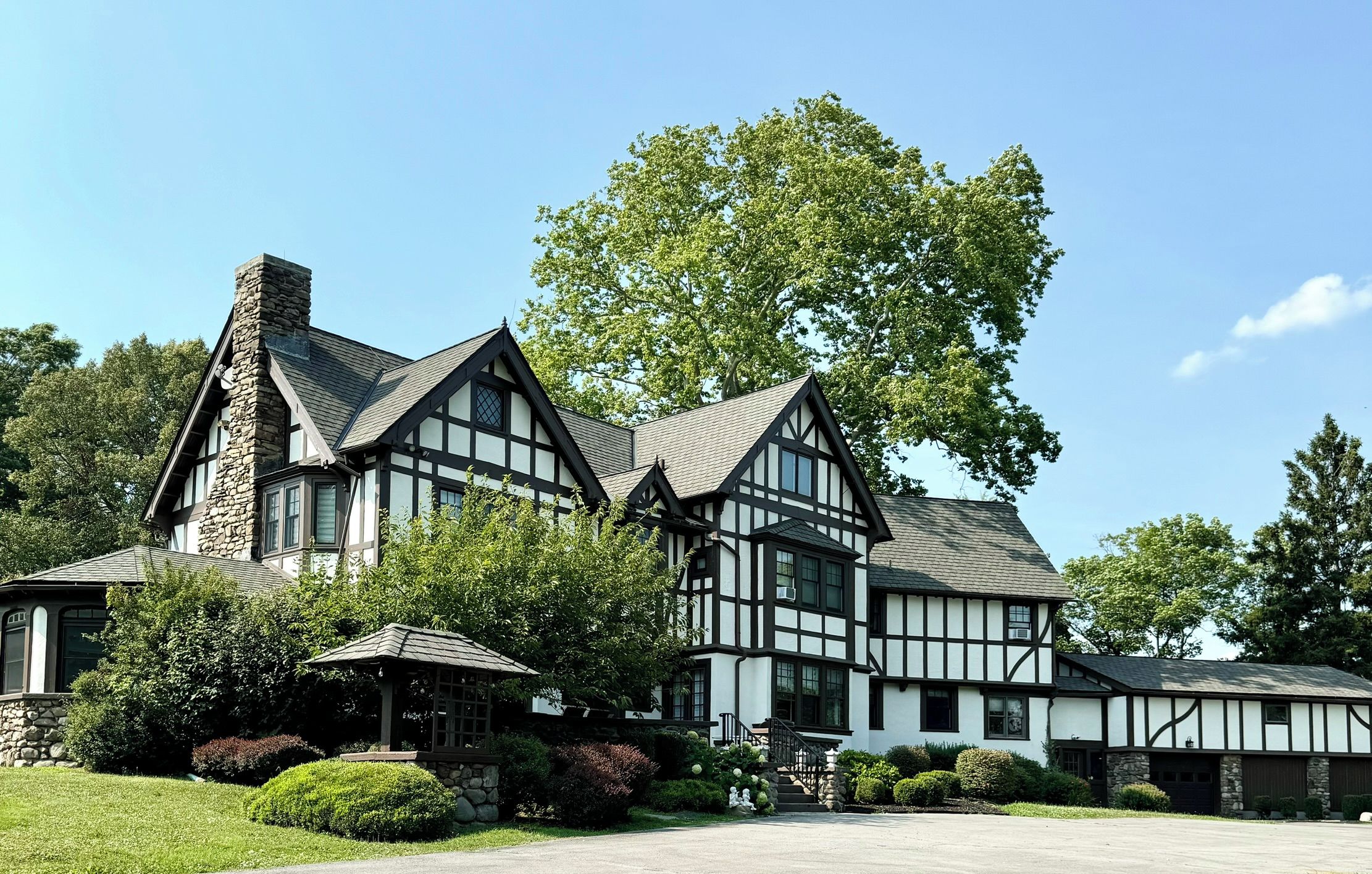 A large, multi-story house with a prominent stone chimney, multiple windows, and a well-maintained garden.
