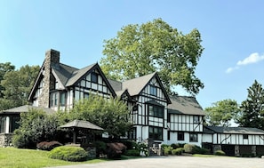 A large, multi-story house with a prominent stone chimney, multiple windows, and a well-maintained garden. - Spectacular Historic Mansion w/Pool&Tennis (Goshen)