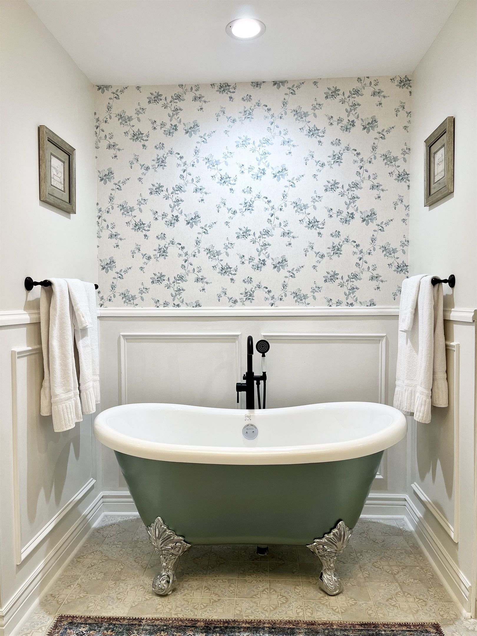 Ein Badezimmer mit freistehender Badewanne, weißen Wänden, floralem Wandpapier und einem gemusterten Boden.