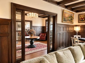 A room with a round table, a red leather chair, a sofa, a chandelier, and two paintings on the wall. - Spectacular Historic Mansion w/Pool&Tennis (Goshen)