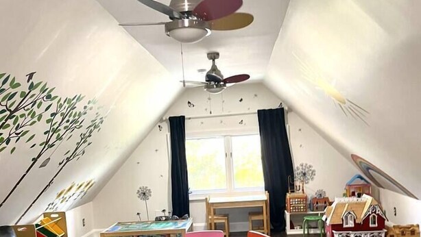 A cozy attic room with a ceiling fan, a colorful play mat, a small dining table with chairs, and a toy house. - Spectacular Historic Mansion w/Pool&Tennis (Goshen)