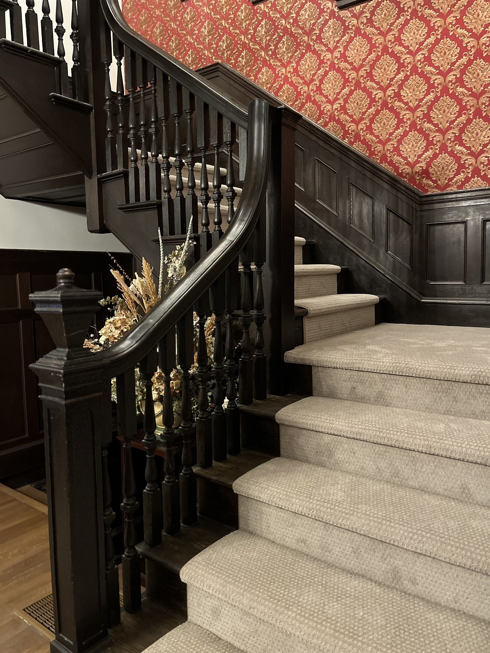 Un magnifique escalier avec des rampes en bois foncé et des marches recouvertes d’une moquette beige.