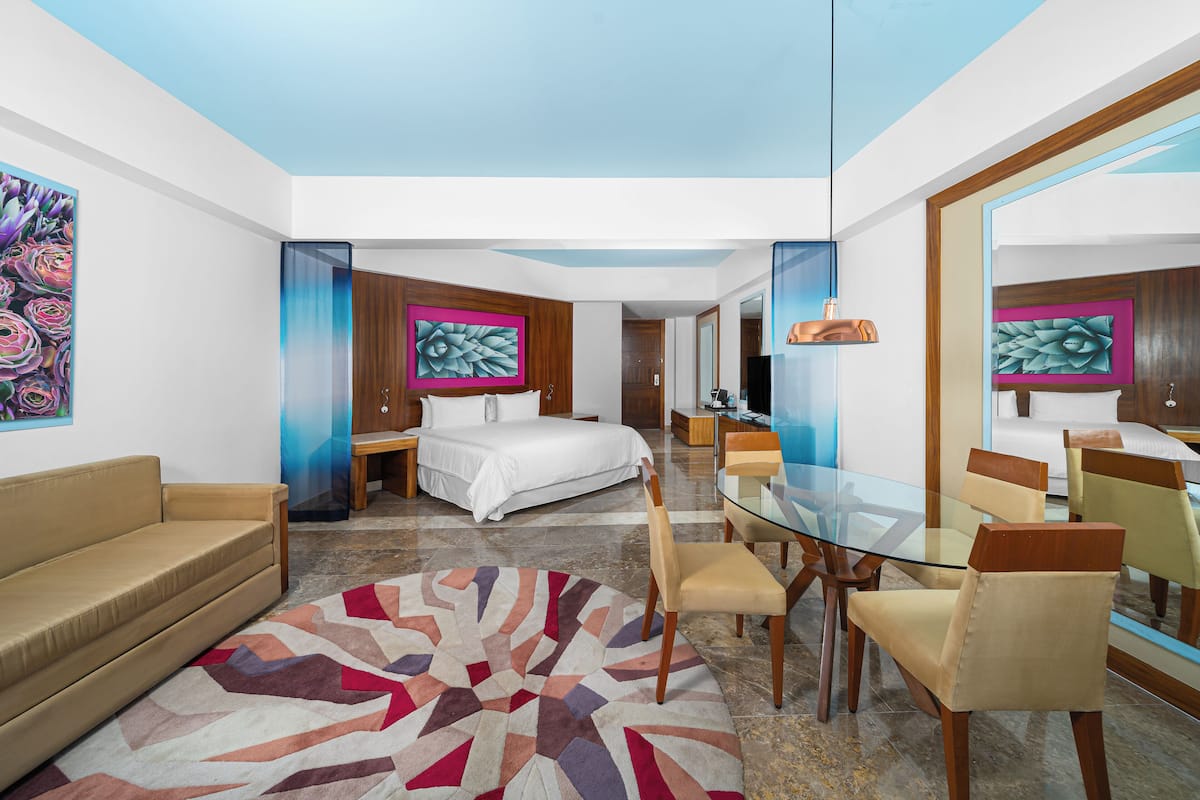 Une chambre d’hôtel moderne avec un lit, une table à manger en verre, un canapé et un grand miroir.