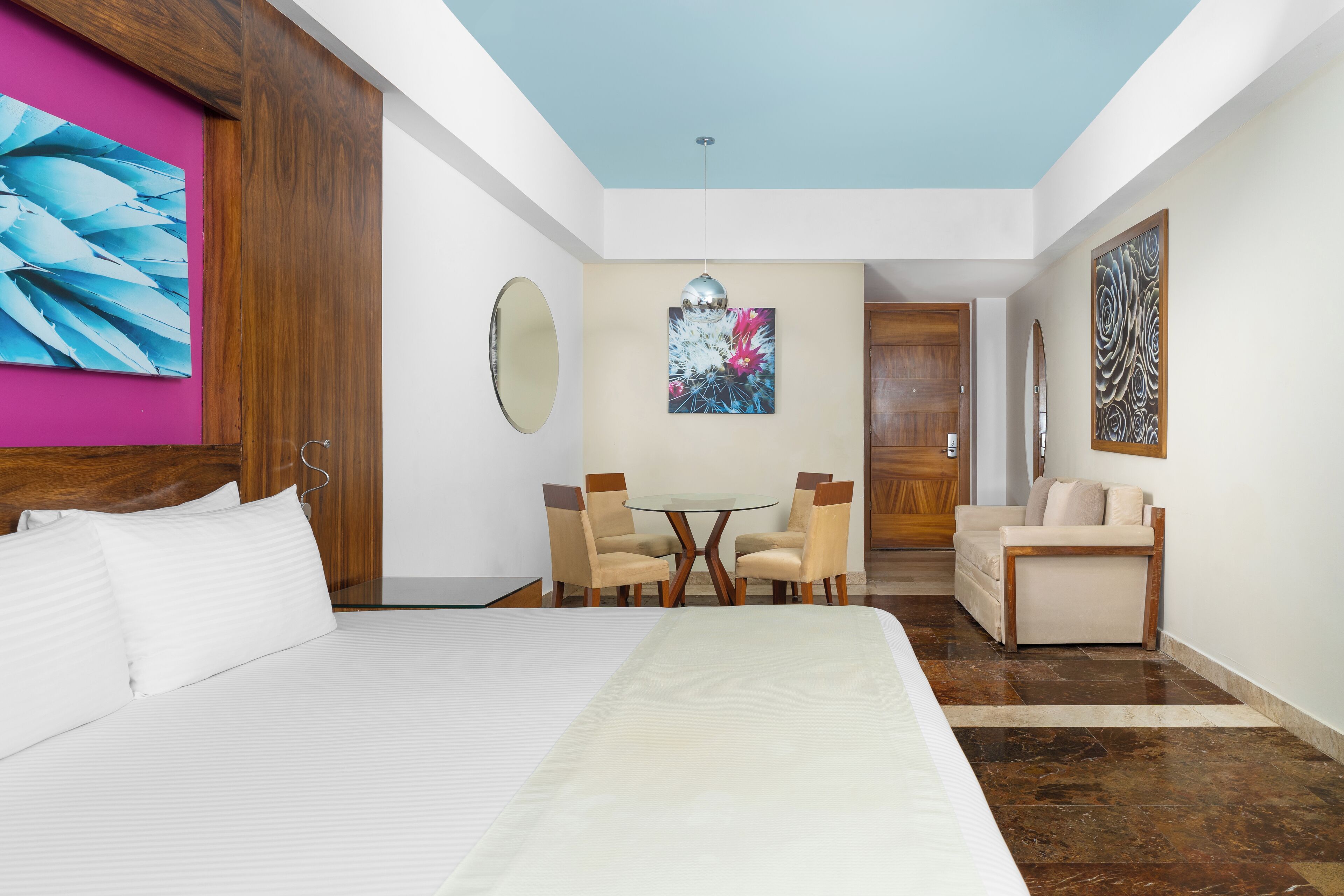 A hotel room with a bed, a desk with chairs, a sofa, and artwork on the walls.