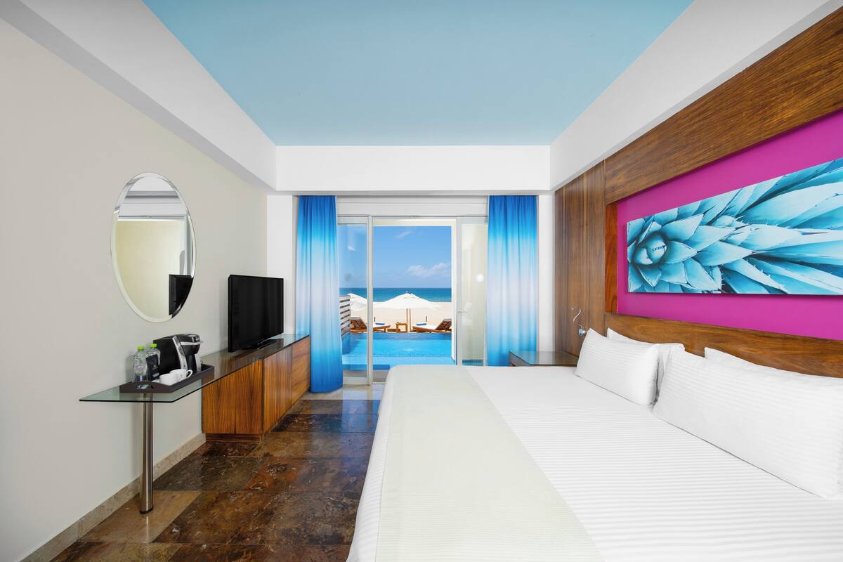 Une chambre d’hôtel avec un lit, une télévision, un bureau avec une machine à café et une vue sur la plage.