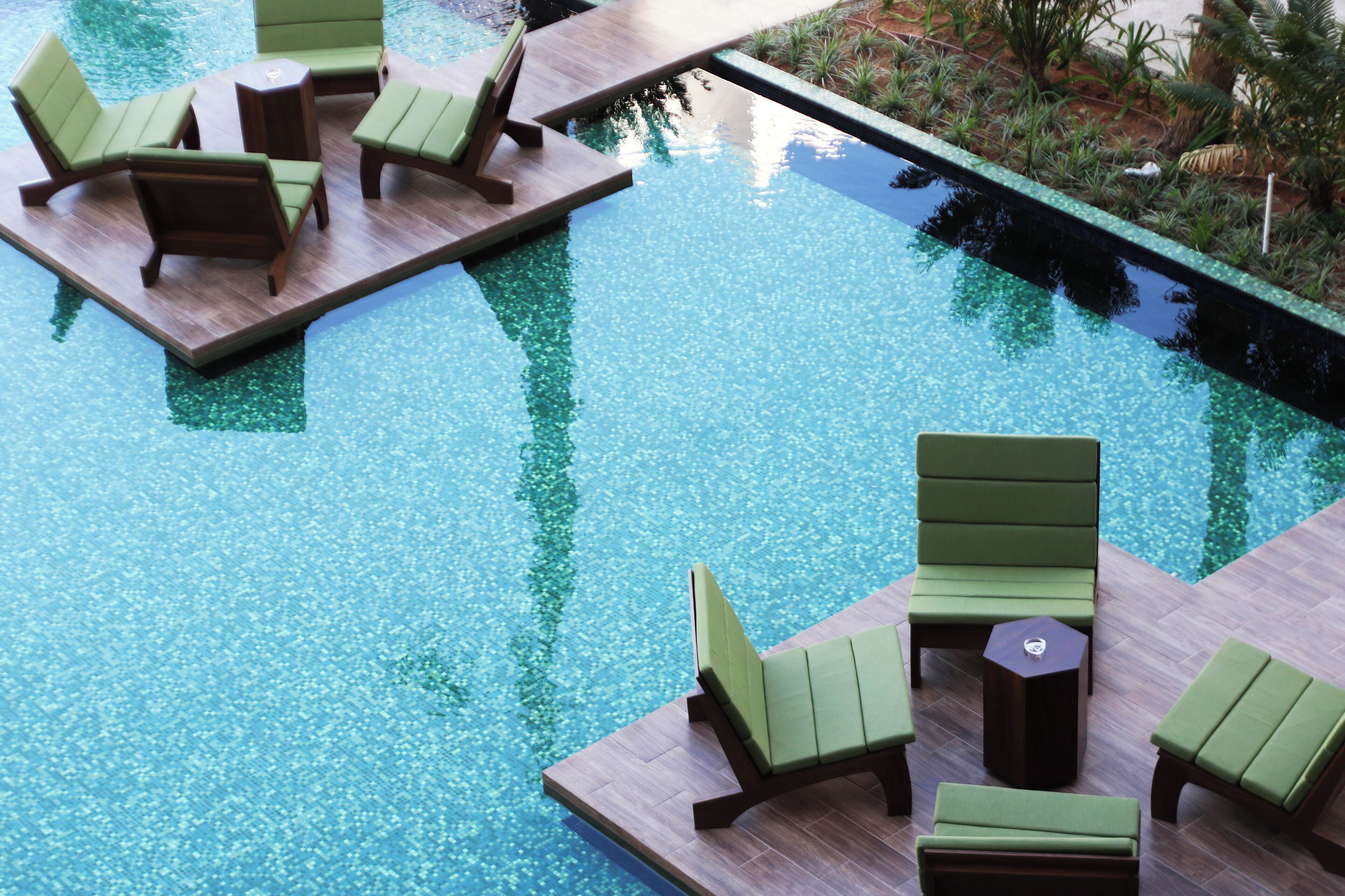 Un espace piscine avec des chaises longues vertes et une petite table.