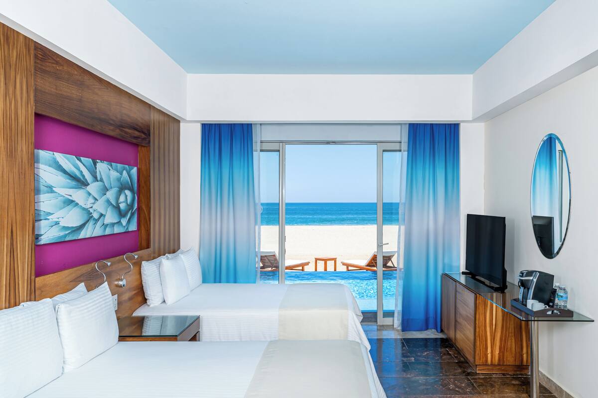 Une chambre d’hôtel avec deux lits, une télévision, un bureau et vue sur la plage.