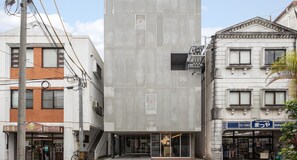 Un bâtiment moderne doté d’une entrée centrale, entouré d’immeubles plus anciens dont les enseignes sont bien visibles.