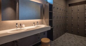 Une salle de bain moderne avec deux lavabos, un grand miroir et une rangée de casiers.